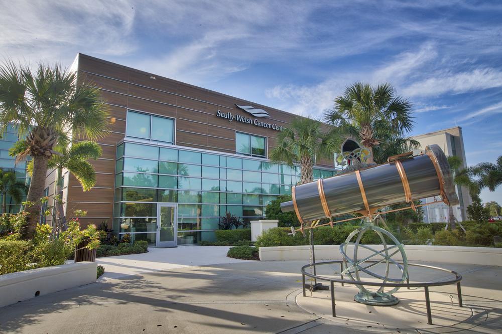 A shot of the Scully Welsh Cancer Center in Florida utilizing Nichiha’s VintageWood fiber cement siding in Cedar. There are palm trees around it, a lot of windows on the building and a large telescope sculpture propped in front.