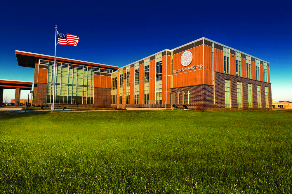 A photo of Racine Dental Group building utilizing Nichiha’s VintageWood fiber cement cladding in Cedar with a grass field in front and an American flag blowing in the wind.