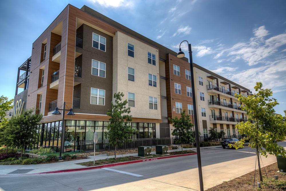 A commercial space (shops and apartment building) featuring an exterior building design with fiber cement siding that’s highlighted by wood and earth tones.