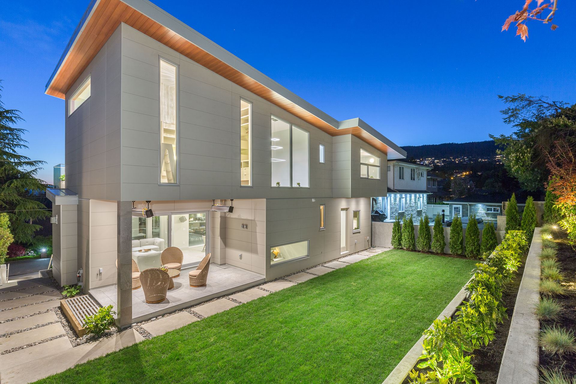 Modern home with bright interior lights and beautiful, green grass and outdoor seating area featuring Nichiha’s ArchBlock panels in gray