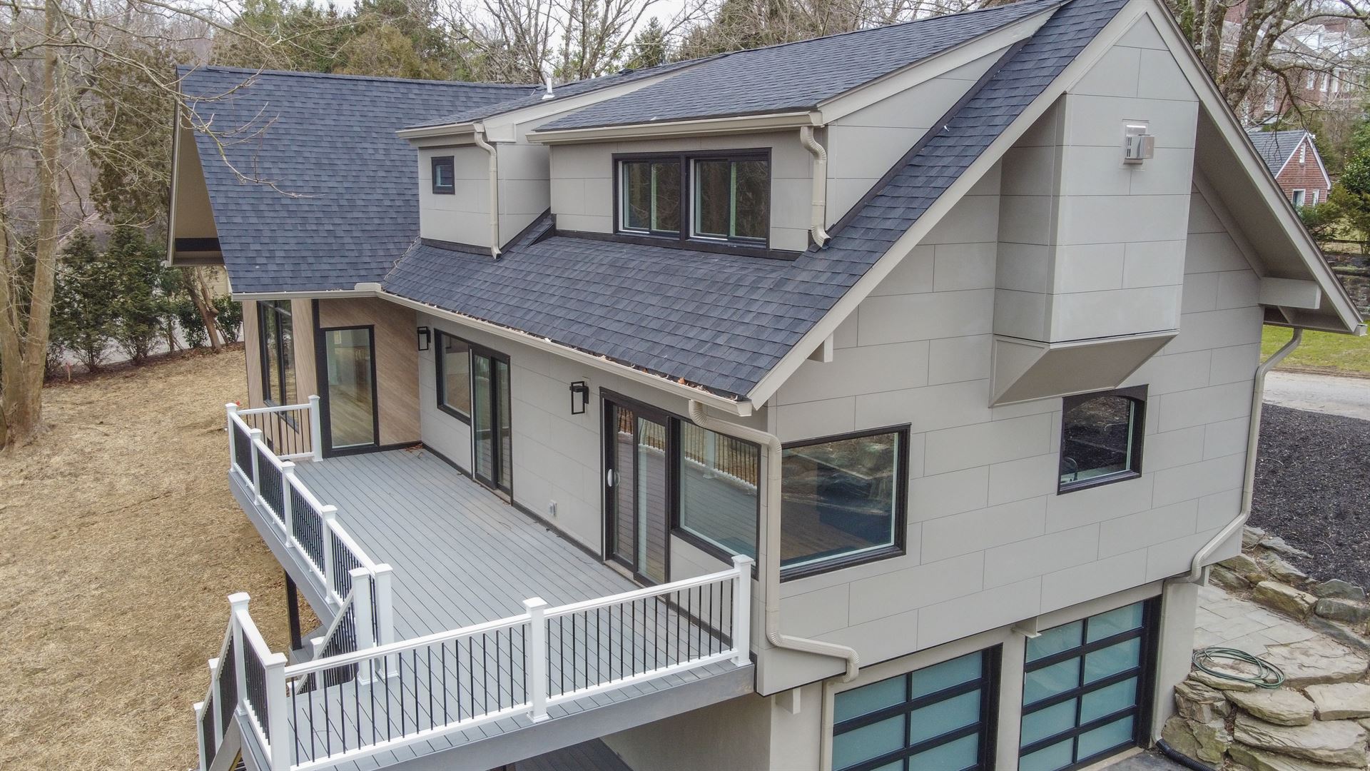 An angled view of the back of a modern-style home featuring gray concrete-textured fiber cement, black trimmed windows and a second-floor porch.