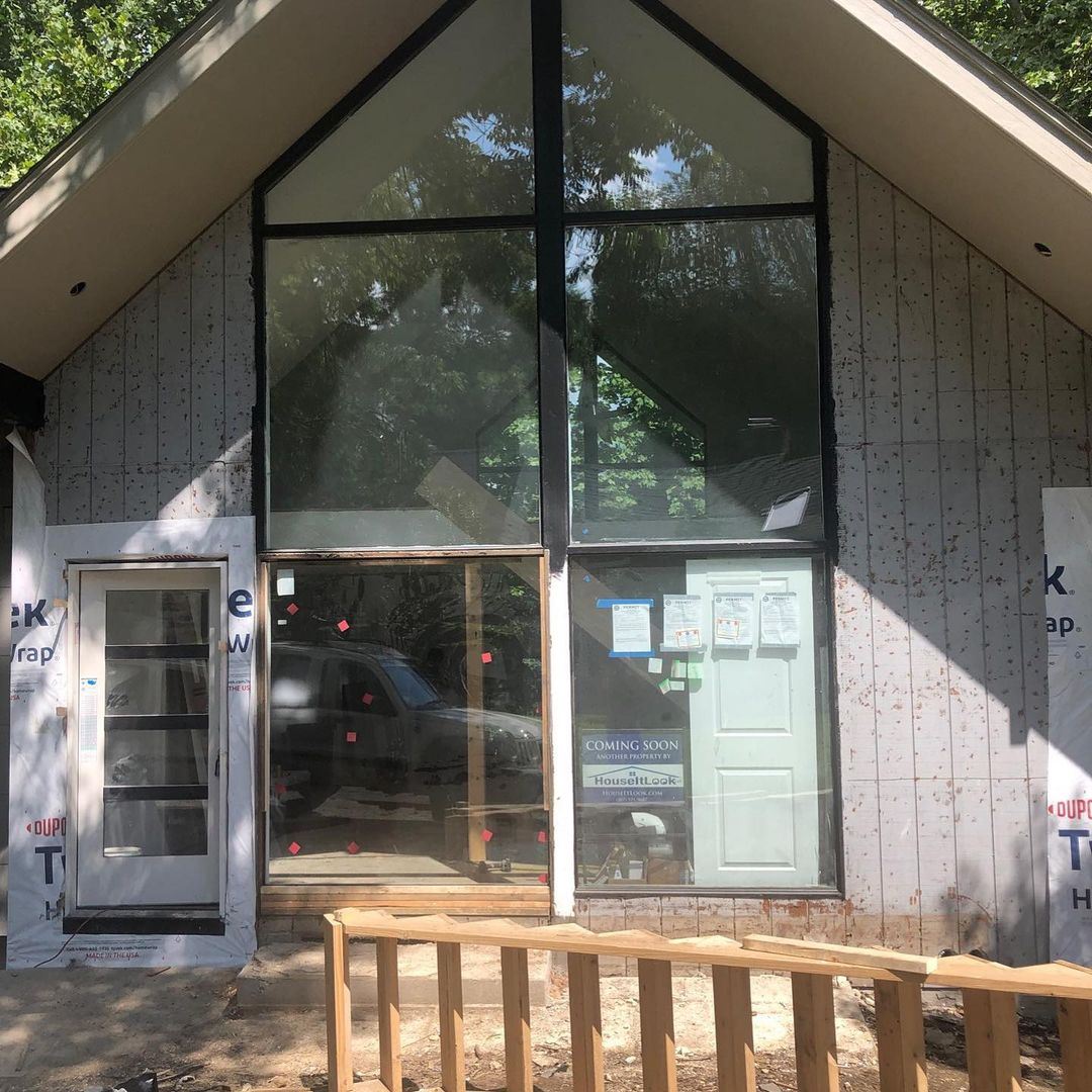 Front, close up view of the home’s front under construction featuring floor to ceiling windows and a peaked roof.