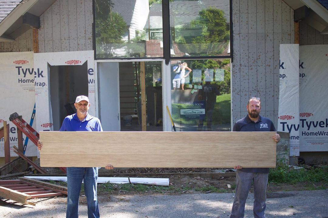 Two men holding a panel of Nichiha VintageWood in front of a home under construction.