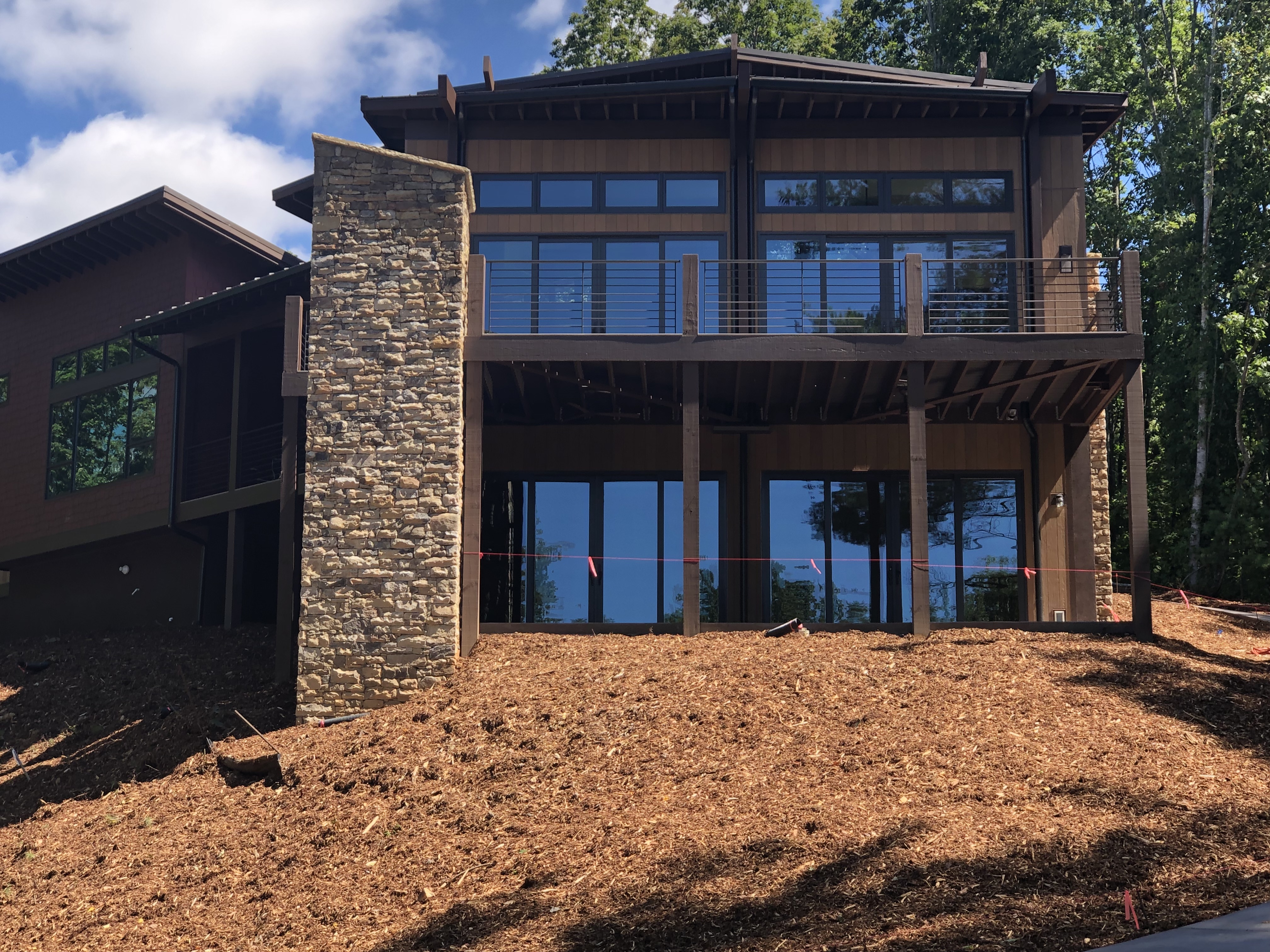 Beautiful two-story home with large porch and balcony that incorporates multiple shades of brown in stone accents and vertical wood-textured fiber cement siding.