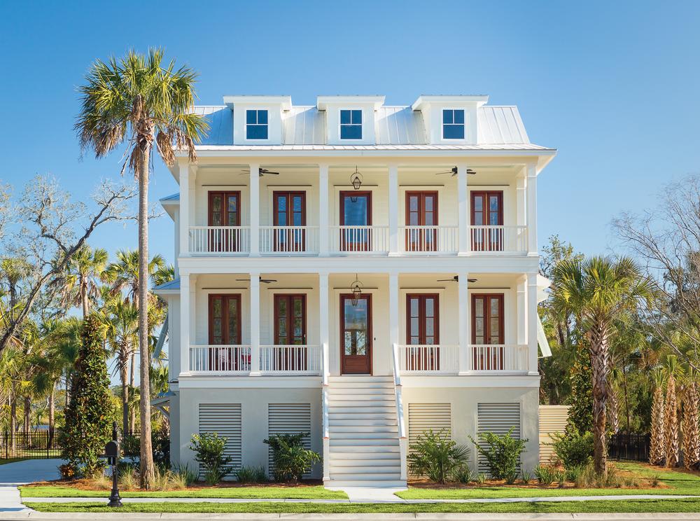 This elevated home has two large front porches. There are two ceiling fans on each of the porches. There are palm trees beside the house.