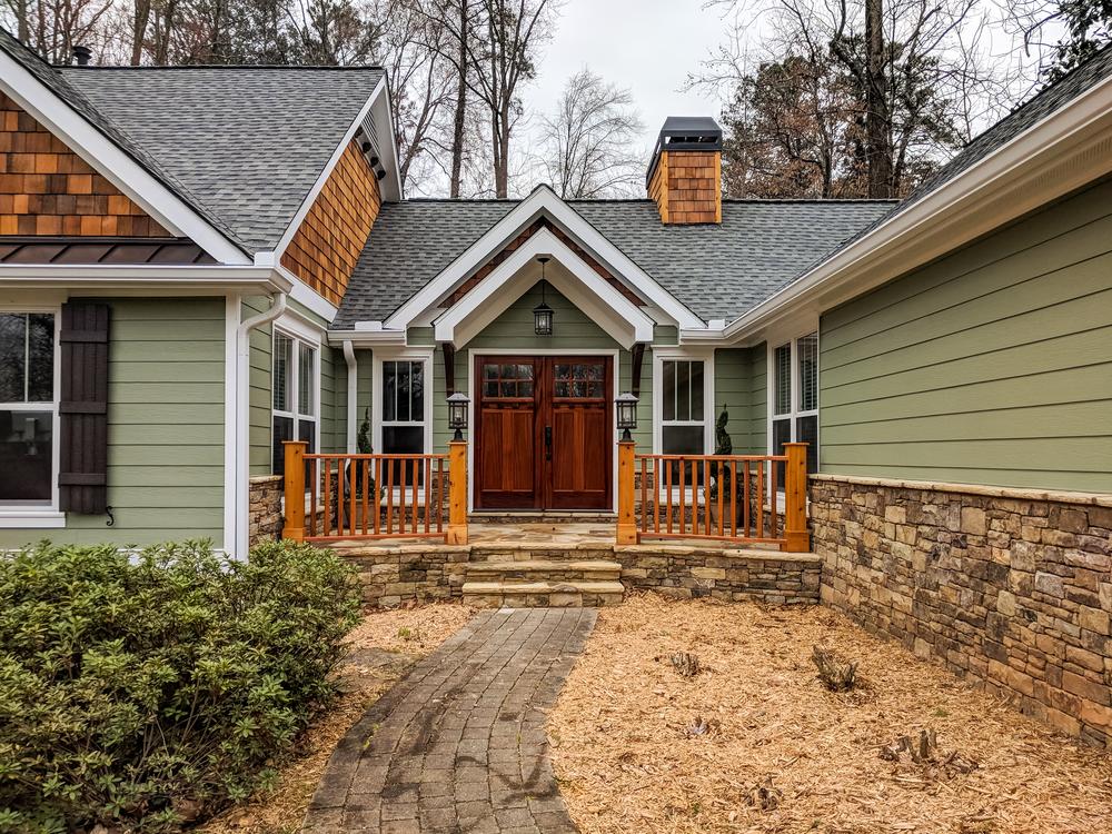 This green home has cedar-like shakes on parts of the home. Stone touches are also incorporated throughout the design. There are two wooden doors as the entrance to the home.