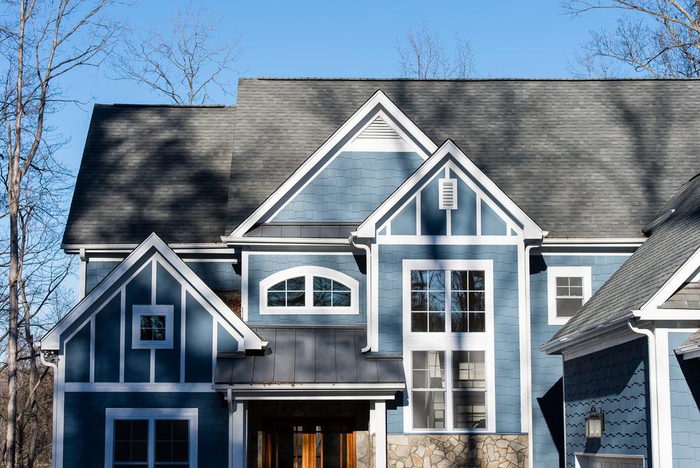 This blue home has staggered siding to create a unique look. There is a stone-like base on one of the walls. The home’s trim is white.