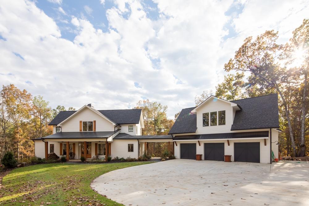 A two-story house with white siding has a three-car garage attached by a roofed walkway. There is a large concrete driveway.