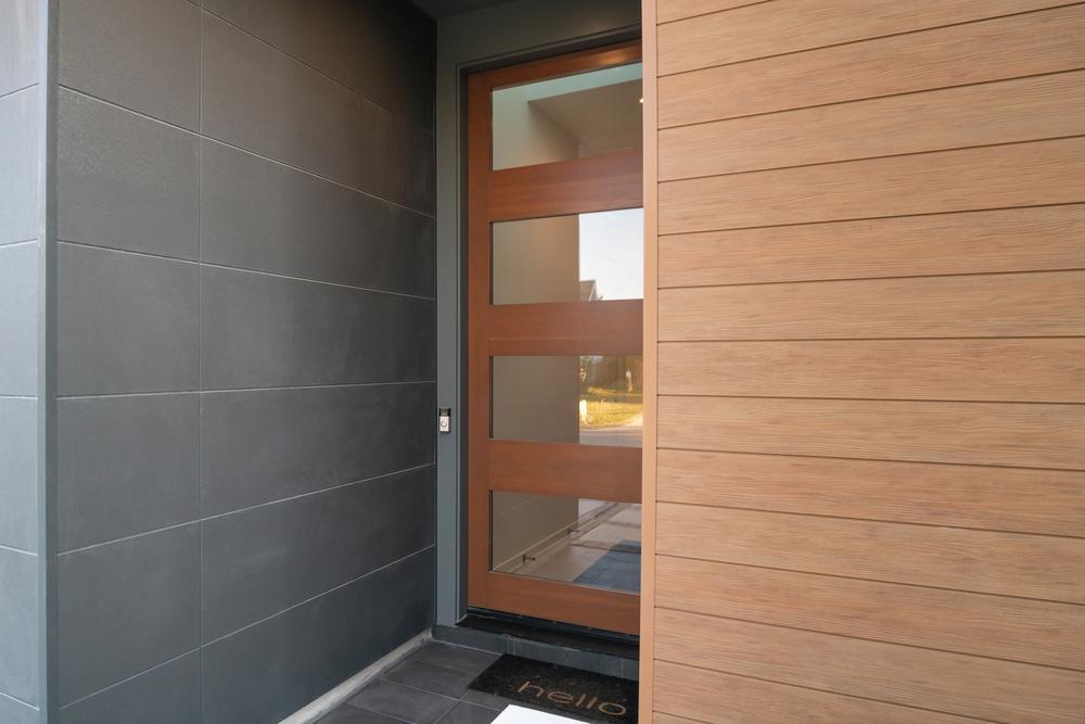 Entryway of a modern home with contrasting wood and concrete fiber cement panels on the exterior of the wall design.