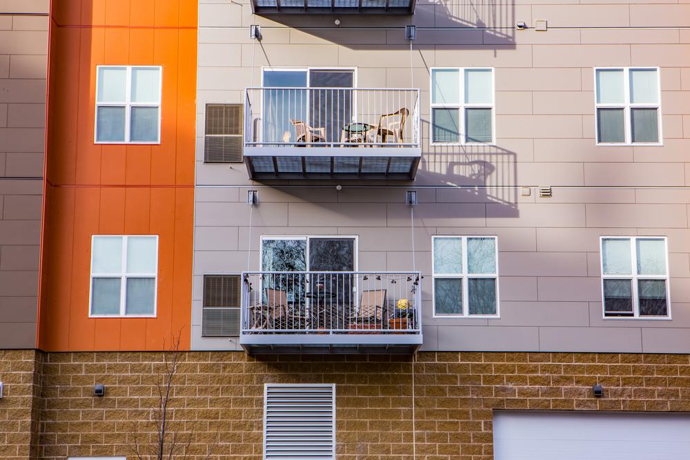This student living building has patio areas for each apartment. There is gray and orange fiber cement siding.