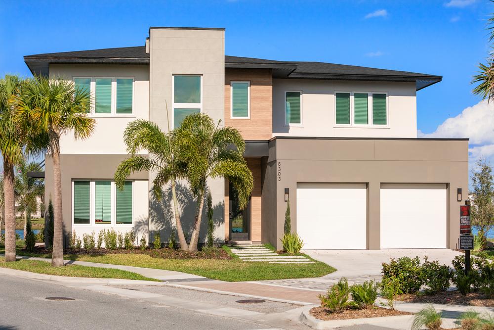 This two-story home has gray, beige and wood-like siding. There are two garage doors and rectangular windows.