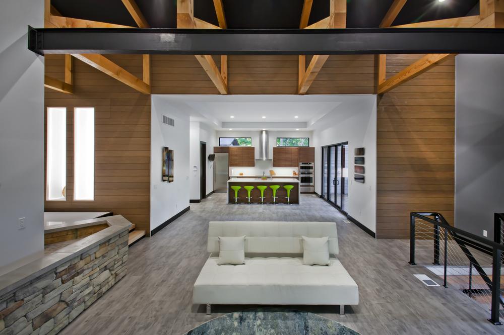 Interior of an open-floor plan home with stone and wood paneling. A living room couch sits in the foreground, and the kitchen is in the background.