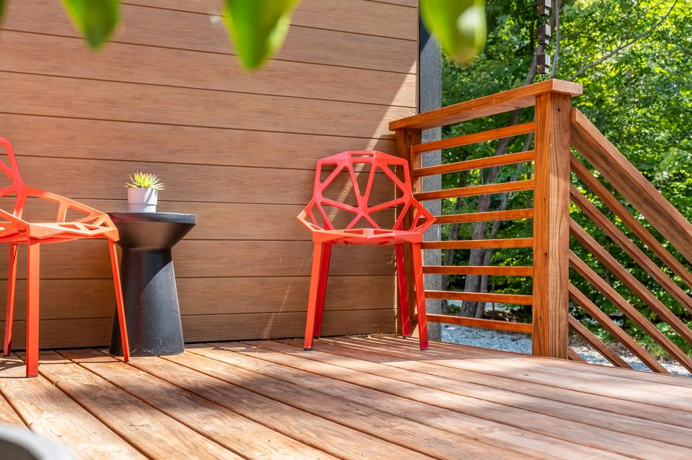A home is protected with Nichiha Vintagewood in cedar. There is a sunny deck area with two red chairs and a black table with a plant.
