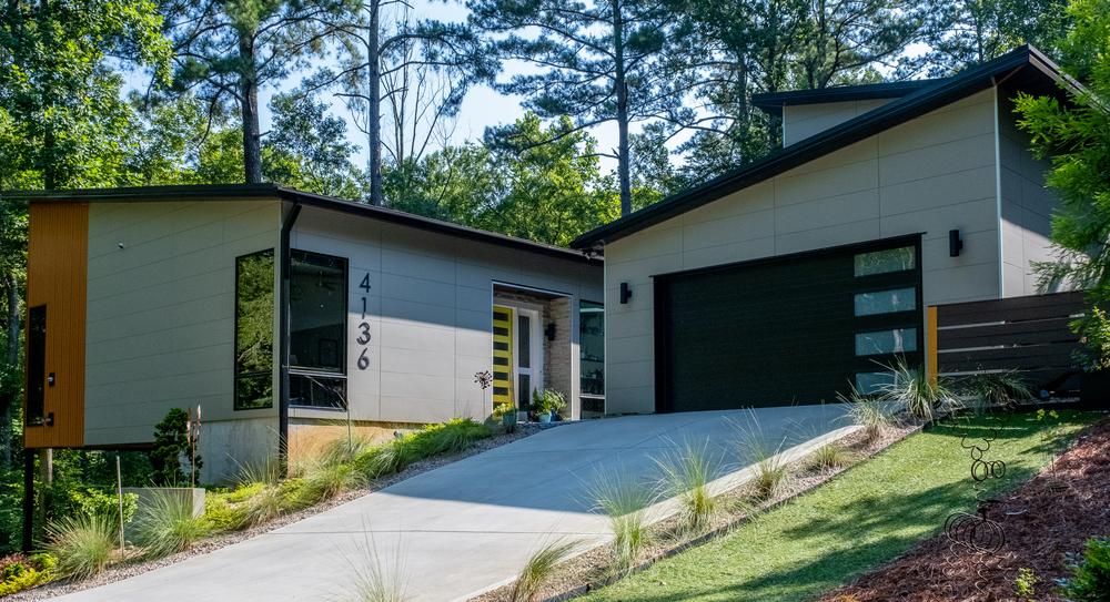 Modern mountain home with gray fiber cement siding panels and grassy lawn with plants.