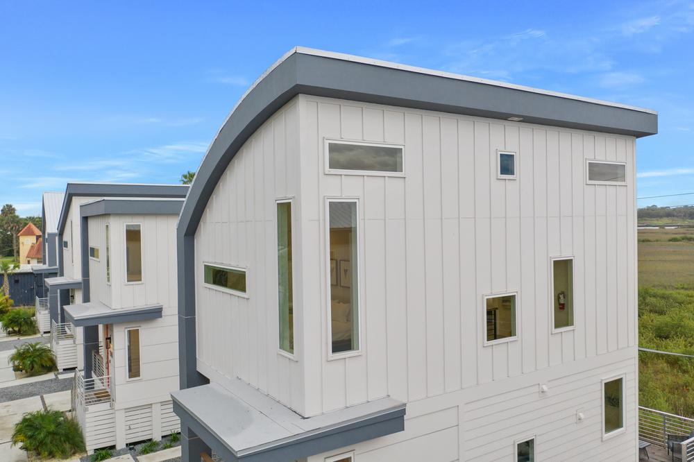 Row of modern beach townhomes with sloped roofs and vertical white fiber cement panel siding.