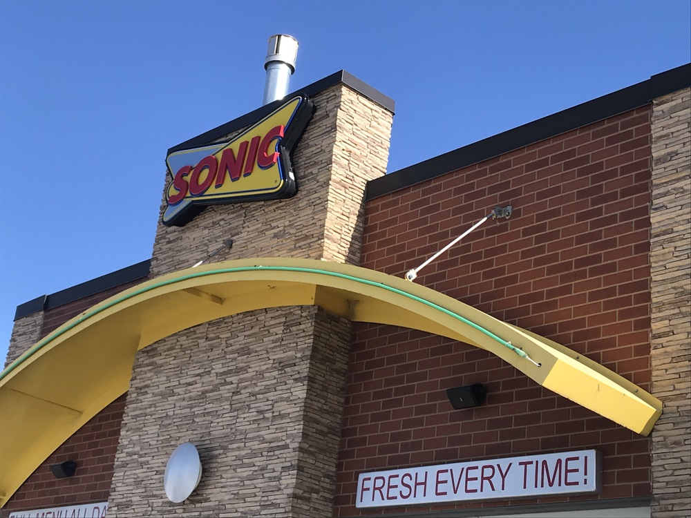 Front of a red brick Sonic drive-through store with stone pillars and a yellow arch.