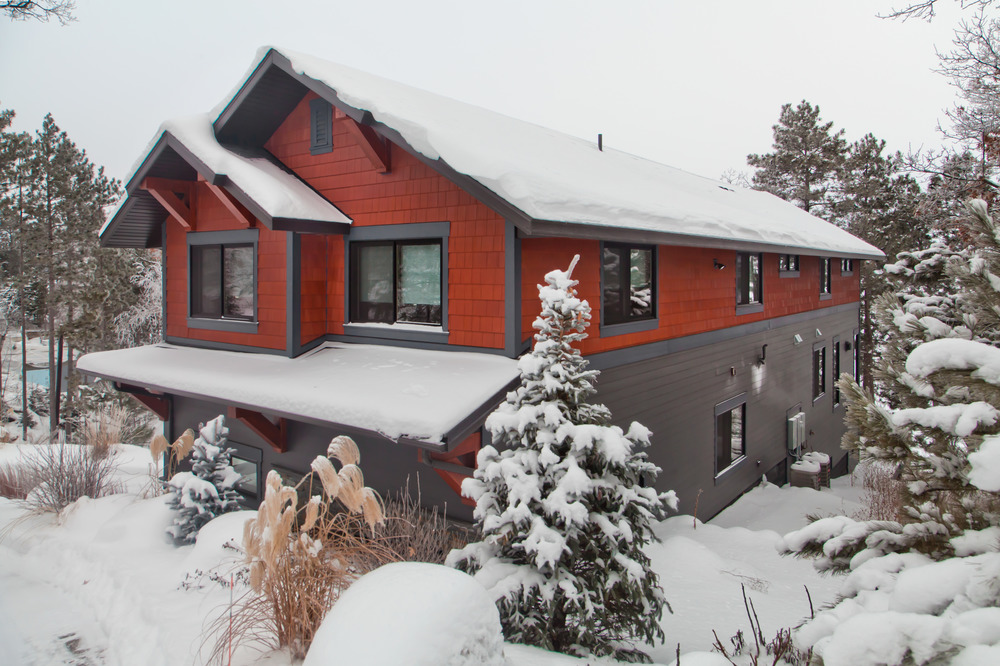This two-story house has an orange shake-style siding on the top half of the house. There is snow on the roof and ground.