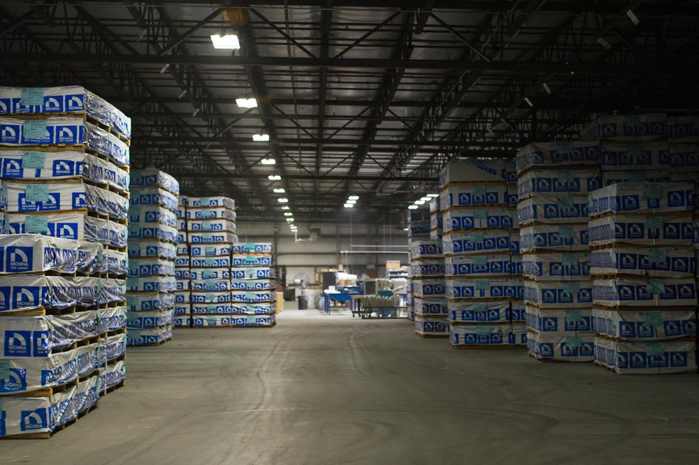A dimly lit warehouse with a walkway surrounded by packaged Nichiha products.