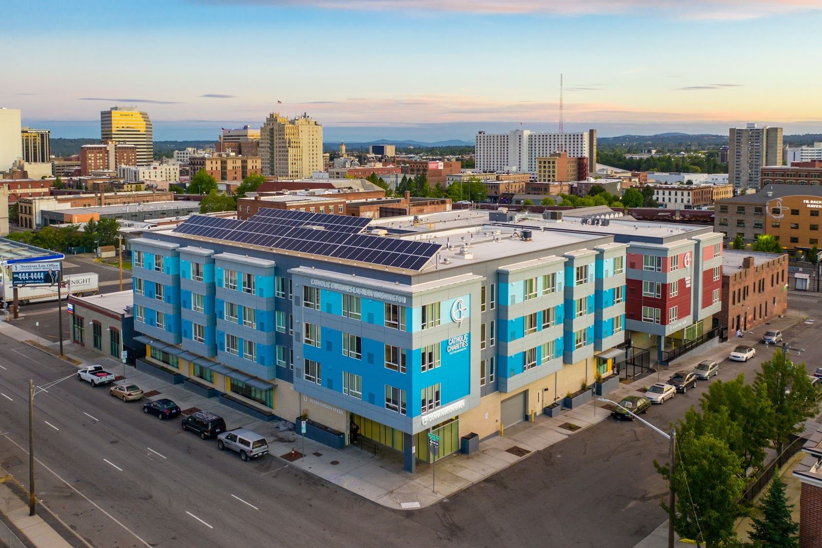 Aerial view of the Jacklin Family Haven building with bright blue cladding and solar panels with the city skyline in the background